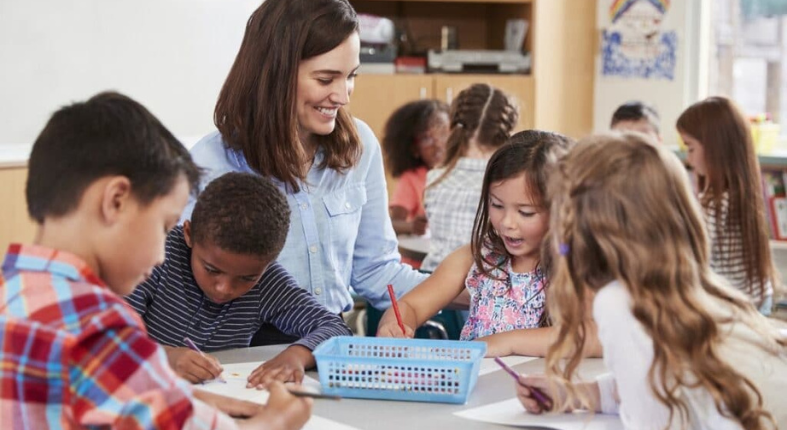 Profesora monitoreando el trabajo en grupo de unos niños y niña en la sala de clases.