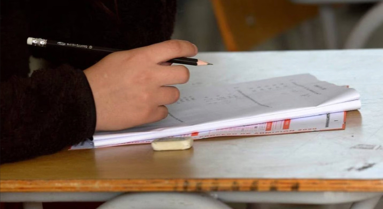 Se observa una mesa donde hay una persona rindiendo la PAES. Solo se ve su mano, la prueba y la mesa.
