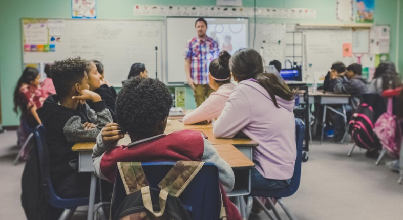Una sala de clases con un profesor haciendo una actividad con estudiantes en grupo.