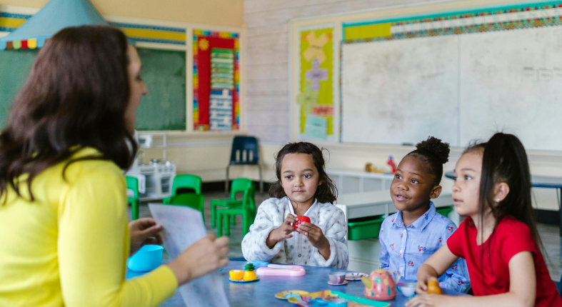 Profesora interactuando con estudiantes en un aula inclusiva y dinámica, fomentando el aprendizaje a través del juego y la participación activa.