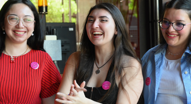 En la imagen se ve a tres estudiantes de pedagogía en primer plano sonriendo.